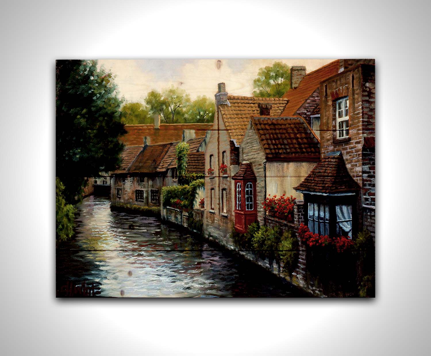 A painting of the Bruges Canal in Belgium, lined by brick homes with red and brown tlie roofs. Red flowers and a red bay window pop in the scene. Printed on a wood pallet.