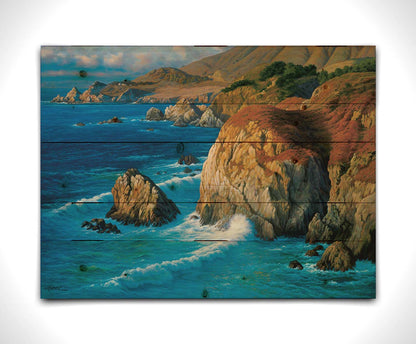 A painting of the rocky cliffsides of Big Sur, California. The vibrant blue waves contrast sharply with the oranges and browns of the grasses on the clifftops. Printed on a wood pallet.