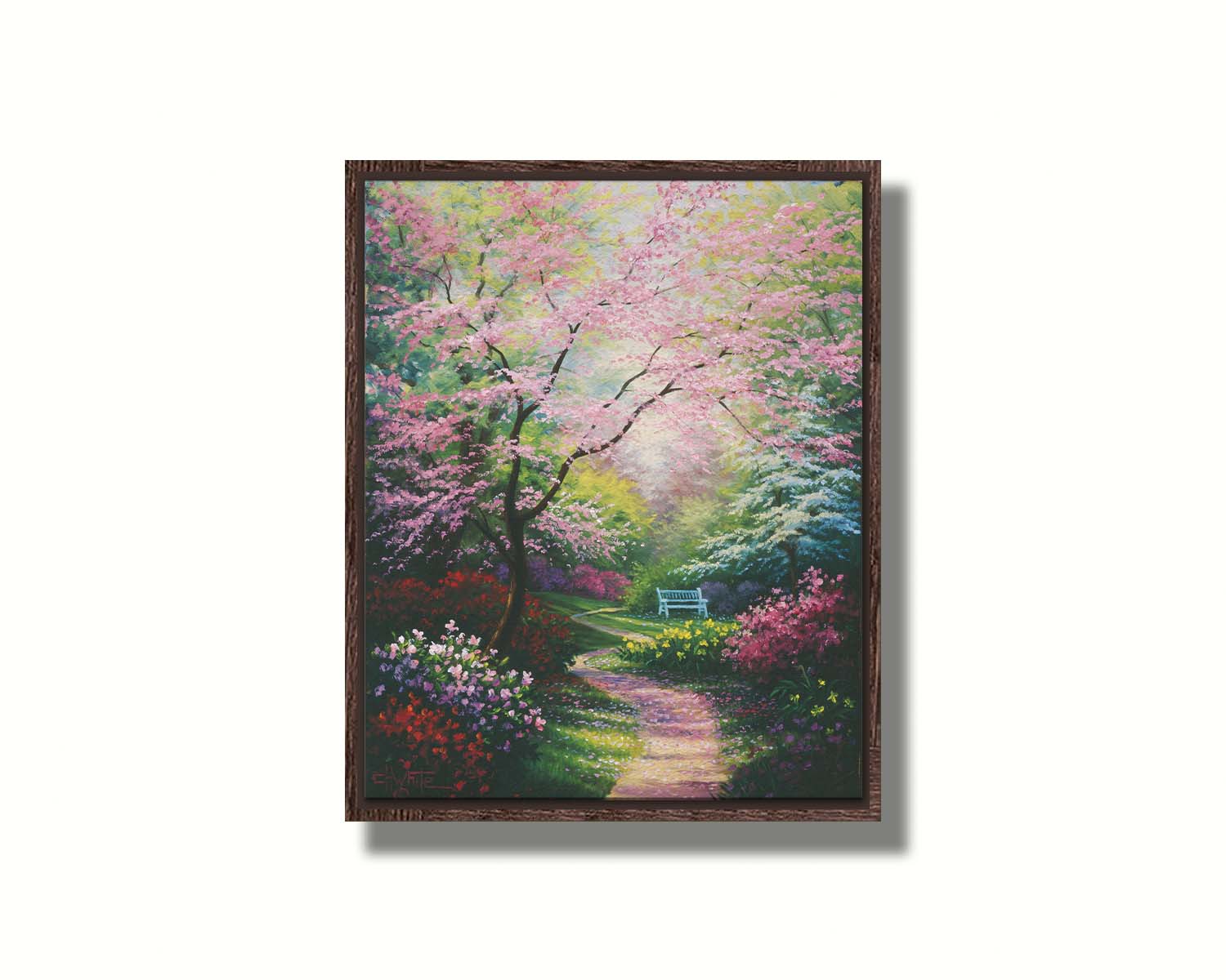 A painting of a garden in spring, with pink, red, and white blossoms on the bushes and trees. Pink petals fall from a tree by the narrow path, piling on the ground. A park bench can be seen in the distance. Printed on canvas in a float frame.