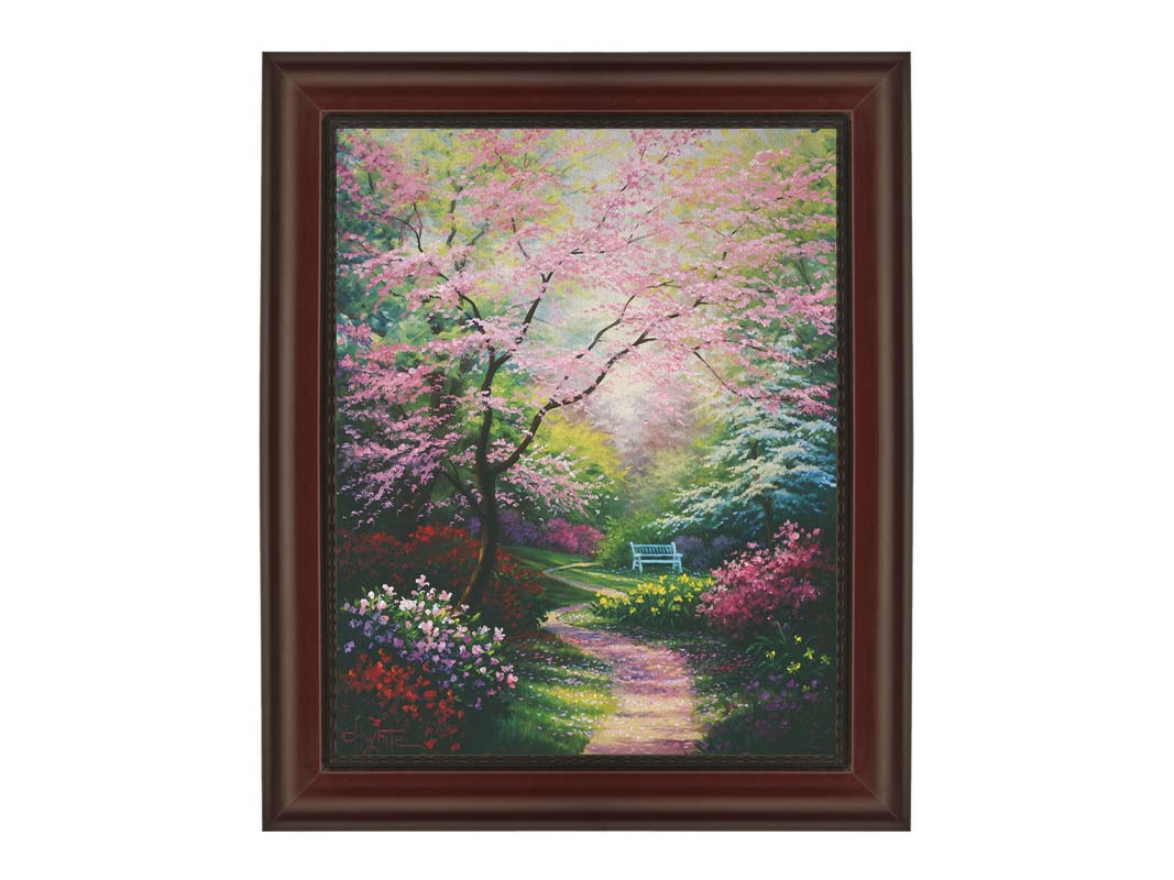 A painting of a garden in spring, with pink, red, and white blossoms on the bushes and trees. Pink petals fall from a tree by the narrow path, piling on the ground. A park bench can be seen in the distance. Printed on canvas and framed.