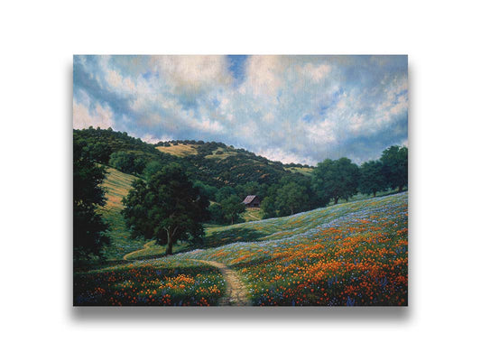 A painting of a hillside meadow of orange and blue flowers. A thin dirt path cuts through the meadow, leading to an old barn in the distance. Printed on canvas.