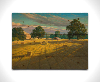 A painting of a field of hay, cut and baled. The vibrant yellows of the grass are highlighted by the warm light of a setting sun. Printed on a wood pallet.