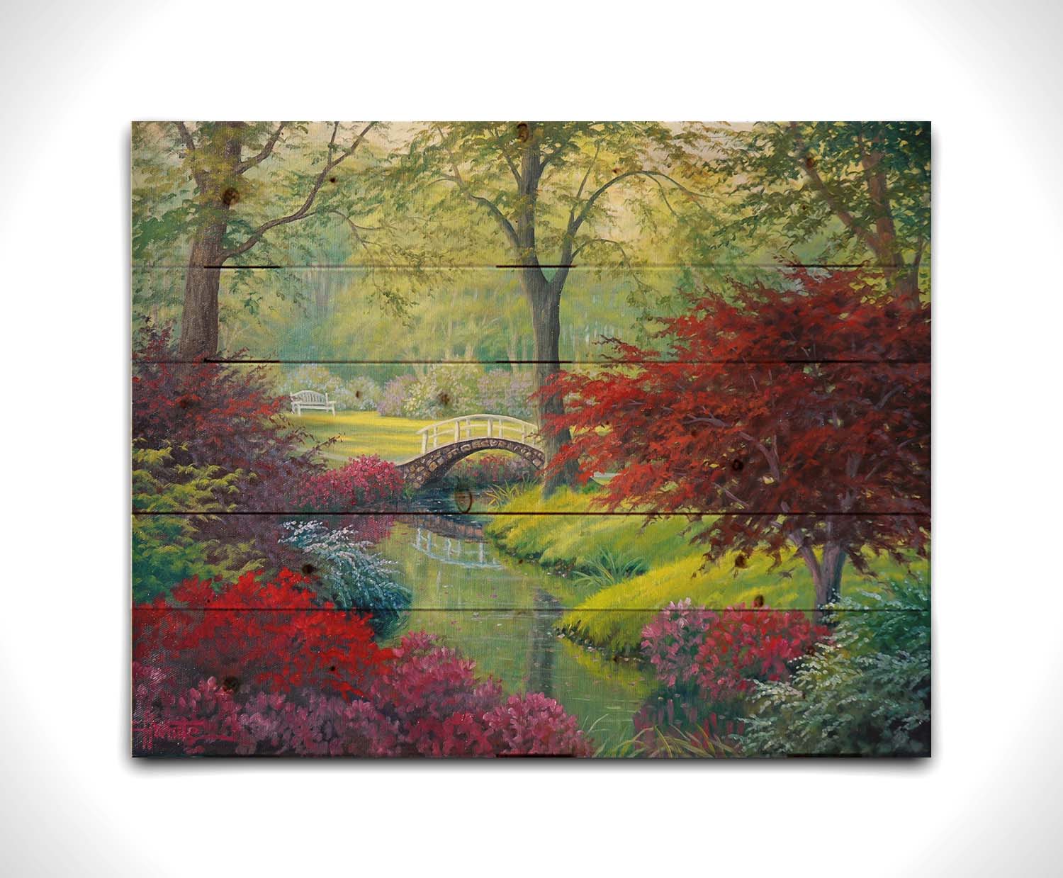 A painting of a garden park, with a stone bridge crossing a stream surrounded by flowering plants. Red, pink, and white flowers stand out against the vibrant greens of the grasses and trees. A white bench can be seen in a grassy clearing in the distance. Printed on a wood pallet.