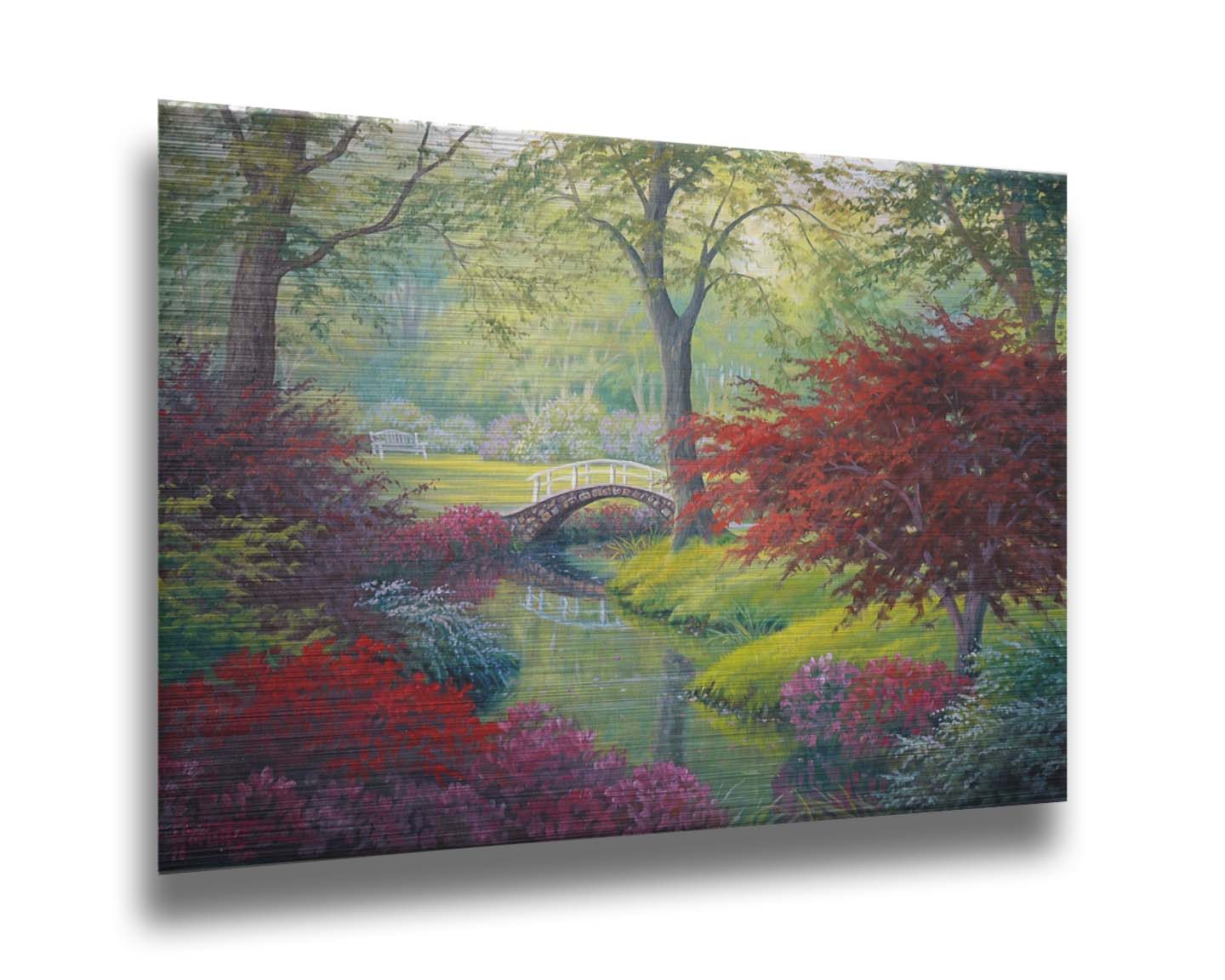 A painting of a garden park, with a stone bridge crossing a stream surrounded by flowering plants. Red, pink, and white flowers stand out against the vibrant greens of the grasses and trees. A white bench can be seen in a grassy clearing in the distance. Printed on metal.