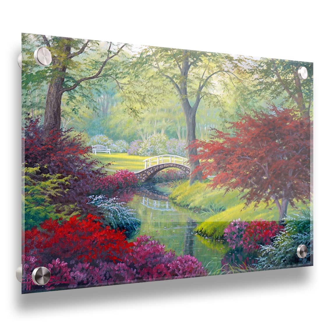 A painting of a garden park, with a stone bridge crossing a stream surrounded by flowering plants. Red, pink, and white flowers stand out against the vibrant greens of the grasses and trees. A white bench can be seen in a grassy clearing in the distance. Printed on acrylic.