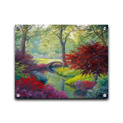 A painting of a garden park, with a stone bridge crossing a stream surrounded by flowering plants. Red, pink, and white flowers stand out against the vibrant greens of the grasses and trees. A white bench can be seen in a grassy clearing in the distance. Printed on acrylic.