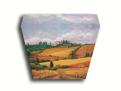 A painting of the Tuscany countryside. All the visible land has been turned eto crop fields, with rows of grape vines in the foreground. On the hills in the distance site a series of white buildings. Printed on canvas.