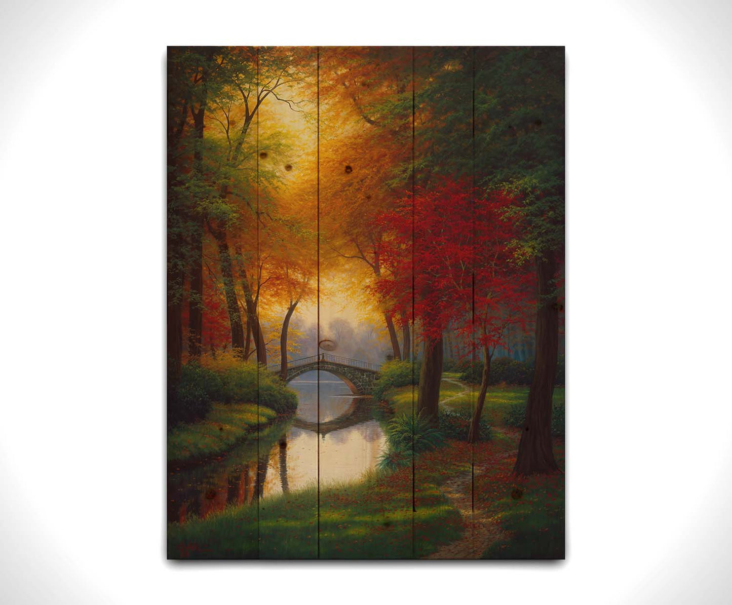 A painting of a path through a forested park in autumn, running alongside a stream to a bridge. Printed on a wood pallet.