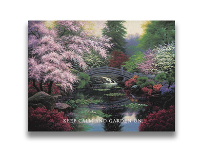 A painting of a tranquil pond surrounded by pink, red, and green flowered trees and shrubs. Lilly pads and fallen pink blossoms float on the water, which is crossed by a wooden bridge.A painting of a tranquil pond surrounded by pink, red, and green flowered trees and shrubs. Lilly pads and fallen pink blossoms float on the water, which is crossed by a wooden bridge. The quote "Keep Calm and Garden On" is overlayed across the bottom. Printed on canvas.