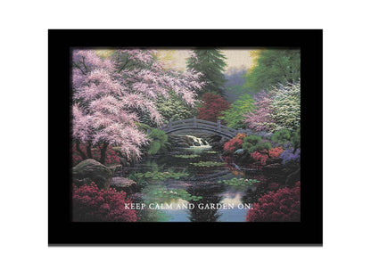 A painting of a tranquil pond surrounded by pink, red, and green flowered trees and shrubs. Lilly pads and fallen pink blossoms float on the water, which is crossed by a wooden bridge.A painting of a tranquil pond surrounded by pink, red, and green flowered trees and shrubs. Lilly pads and fallen pink blossoms float on the water, which is crossed by a wooden bridge. The quote "Keep Calm and Garden On" is overlayed across the bottom. Printed on canvas and framed.