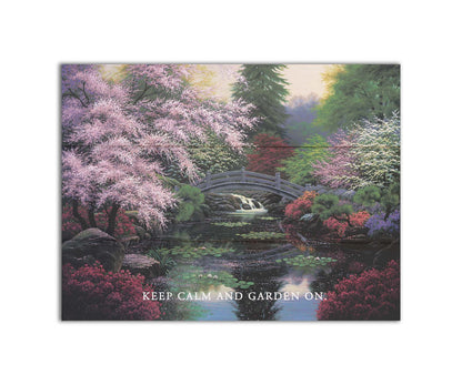 A painting of a tranquil pond surrounded by pink, red, and green flowered trees and shrubs. Lilly pads and fallen pink blossoms float on the water, which is crossed by a wooden bridge.A painting of a tranquil pond surrounded by pink, red, and green flowered trees and shrubs. Lilly pads and fallen pink blossoms float on the water, which is crossed by a wooden bridge. The quote "Keep Calm and Garden On" is overlayed across the bottom. Printed on a box board.