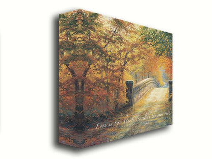 A painting looking down a bridge road during fall. The trees lining the road have turned yellow and orange for autumn, and some of their fallen leaves are scatted along the path. The quote "Love is two hearts traveling the same road" is overlayed across the image in white. Printed on canvas.