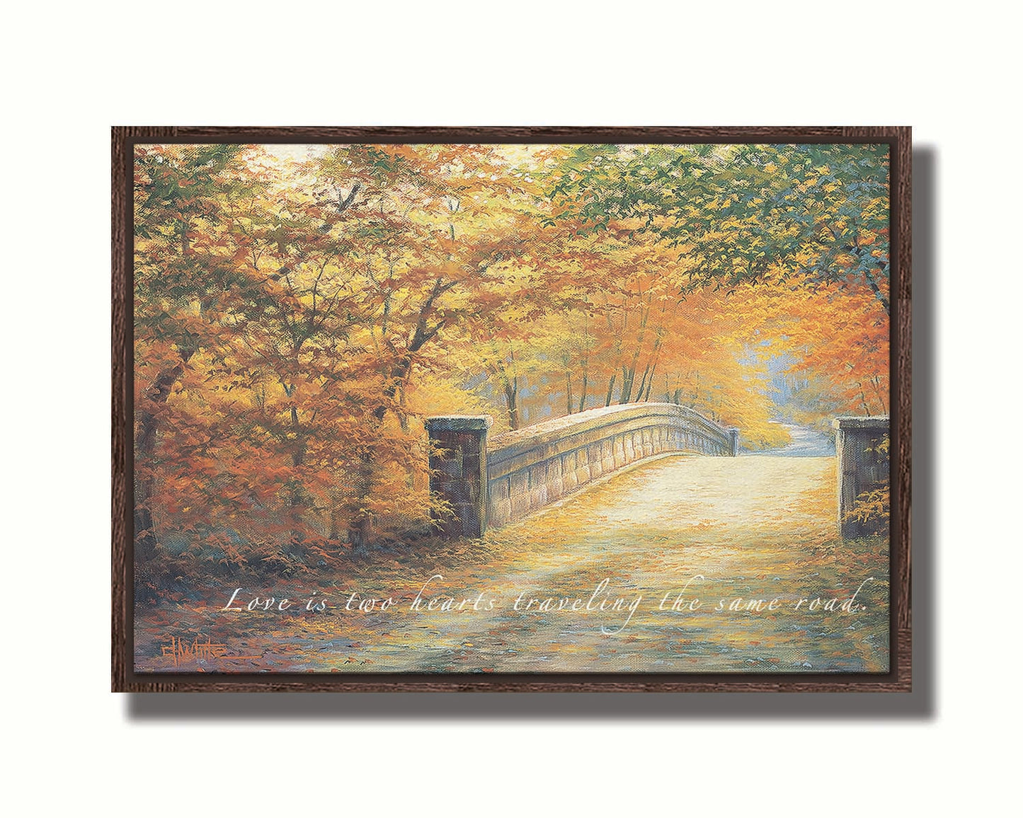 A painting looking down a bridge road during fall. The trees lining the road have turned yellow and orange for autumn, and some of their fallen leaves are scatted along the path. The quote "Love is two hearts traveling the same road" is overlayed across the image in white. Printed on canvas in a float frame.