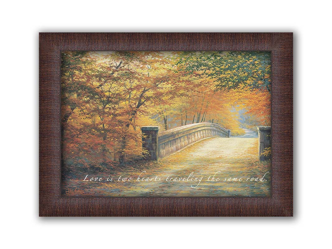 A painting looking down a bridge road during fall. The trees lining the road have turned yellow and orange for autumn, and some of their fallen leaves are scatted along the path. The quote "Love is two hearts traveling the same road" is overlayed across the image in white. Printed on canvas and framed.