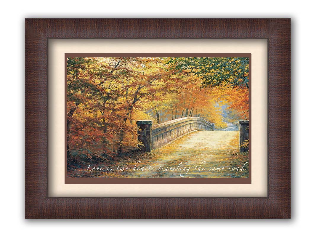 A painting looking down a bridge road during fall. The trees lining the road have turned yellow and orange for autumn, and some of their fallen leaves are scatted along the path. The quote "Love is two hearts traveling the same road" is overlayed across the image in white. Printed on paper, matted, and framed.