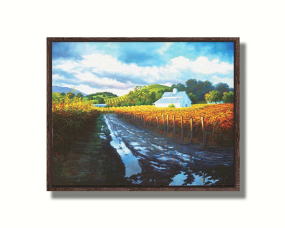 A painting looking down a road puddled with water. On either side, orange, red, and yellow grape vines grow in the vineyard. White barns and houses sit between the fields. Printed on canvas in a float frame.