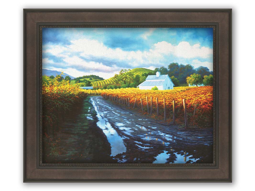 A painting looking down a road puddled with water. On either side, orange, red, and yellow grape vines grow in the vineyard. White barns and houses sit between the fields. Printed on canvas and framed.