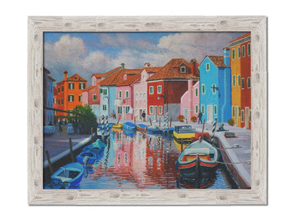 A painting of a canal in the Murano islands in Italy. Several small boats are docked along the sides, and bright, colorful buildings line the paths. Printed on canvas and framed.