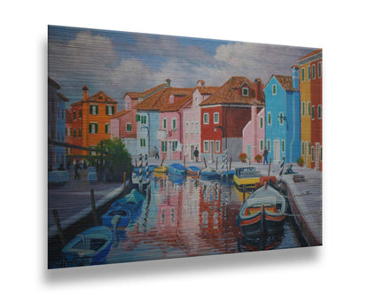 A painting of a canal in the Murano islands in Italy. Several small boats are docked along the sides, and bright, colorful buildings line the paths. Printed on metal.