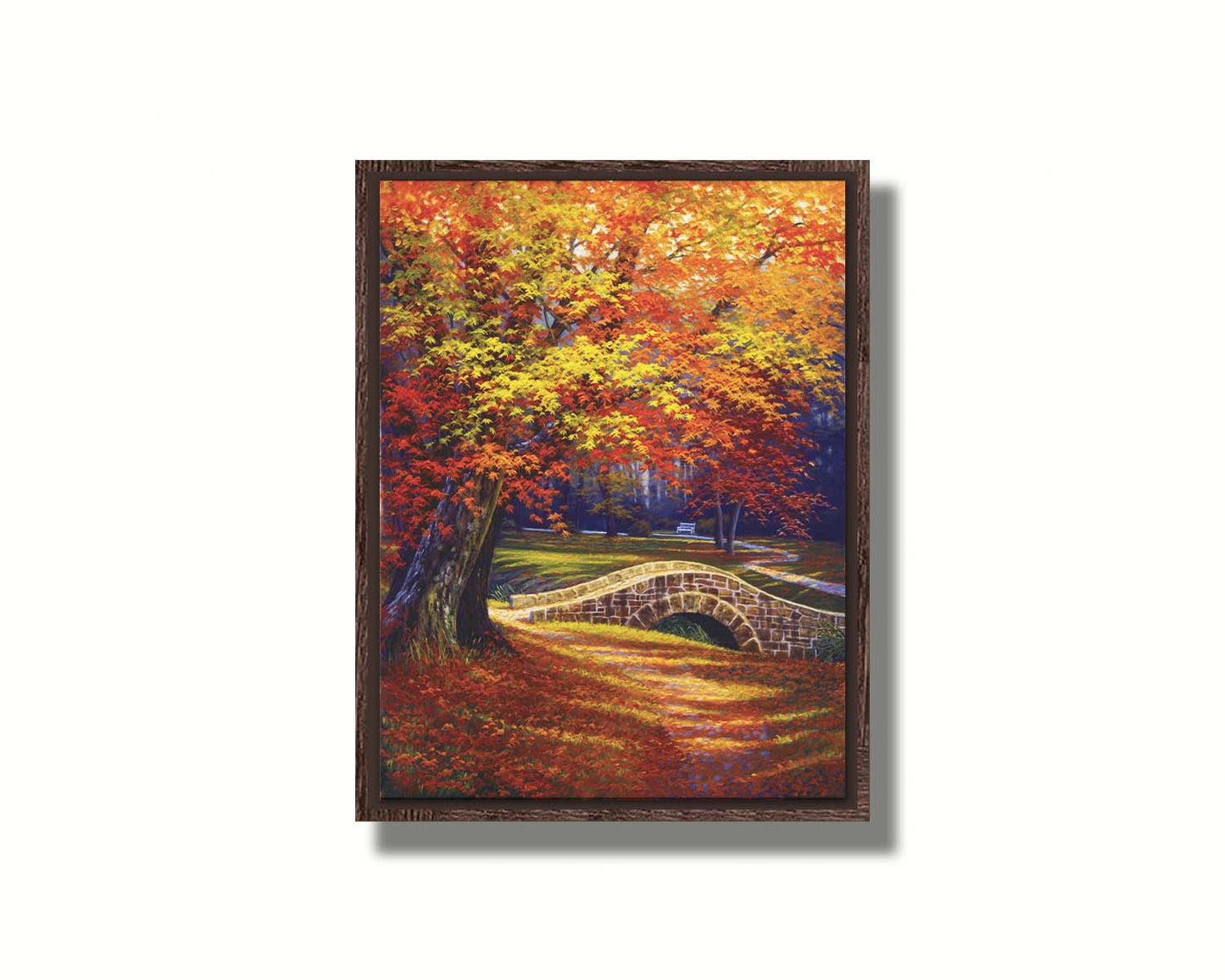 A painting of an autumn park, with the colorful trees dropping orange leaves onto the path below. A stone bridge crosses a small stream. Printed on canvas in a float frame.