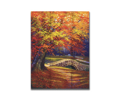 A painting of an autumn park, with the colorful trees dropping orange leaves onto the path below. A stone bridge crosses a small stream. Printed on a box board.