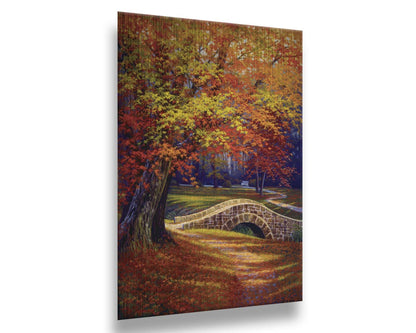 A painting of an autumn park, with the colorful trees dropping orange leaves onto the path below. A stone bridge crosses a small stream. Printed on metal.