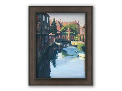 A painting of a canal in Canterbury in Kent, England. A few small row boats are docked along the waterway between historic red brick buildings. Printed on canvas and framed.