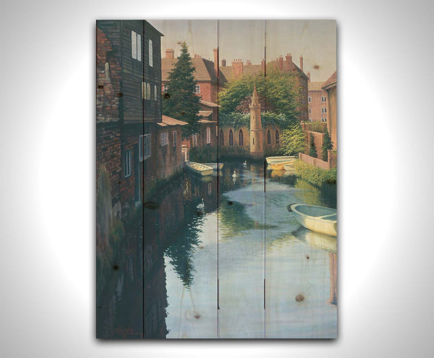 A painting of a canal in Canterbury in Kent, England. A few small row boats are docked along the waterway between historic red brick buildings. Printed on a wood pallet.