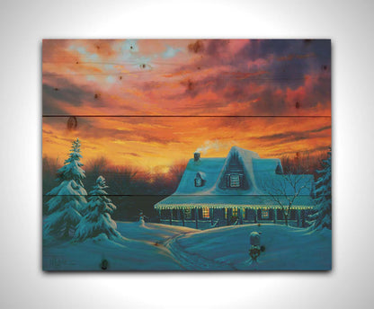 A painting of a house, decorated for Christmas, covered in and surrounded by snow. The sun sets in the background, warming the scene in spite of the weather. Printed on a wood pallet.