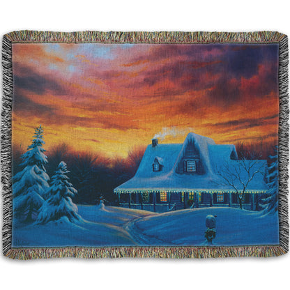 A woven throw blanket designed with a painting of a house, decorated for Christmas, covered in and surrounded by snow.