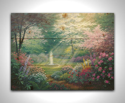 A painting of a garden filled with a variety of flowers, including lavender and poppies, alongside blooming pink and white trees. A fountain is at the garden's center, lit by beams of light from between the trees. Doves fly through the scene. Printed on a wood pallet.