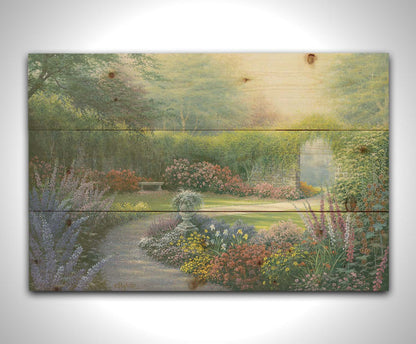 A painting of a path through a garden, filled with flowers in every color– including irises, foxgloves, butterfly bush, and more. A vine-covered stone wall with an archway surrounds the area. Printed on a wood pallet.