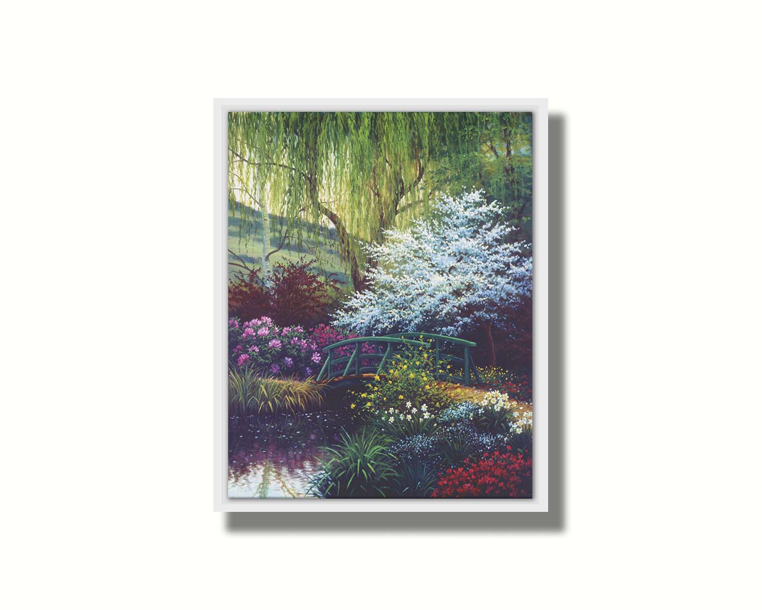 A painting of Claude Monet’s iconic water lily pond in Giverny, France, featuring a small bridge over the canal that brings water into the pond. It is surrounded by willow trees, trees with white and red blossoms, and a variety of flowers. Printed on canvas in a float frame.