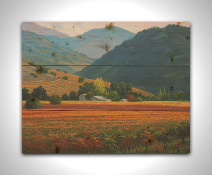 A landscape painting of the Napa Valley wine region in California. Colorful orange, red, and green vineyards are nestled among forested mountains. Printed on a wood pallet.