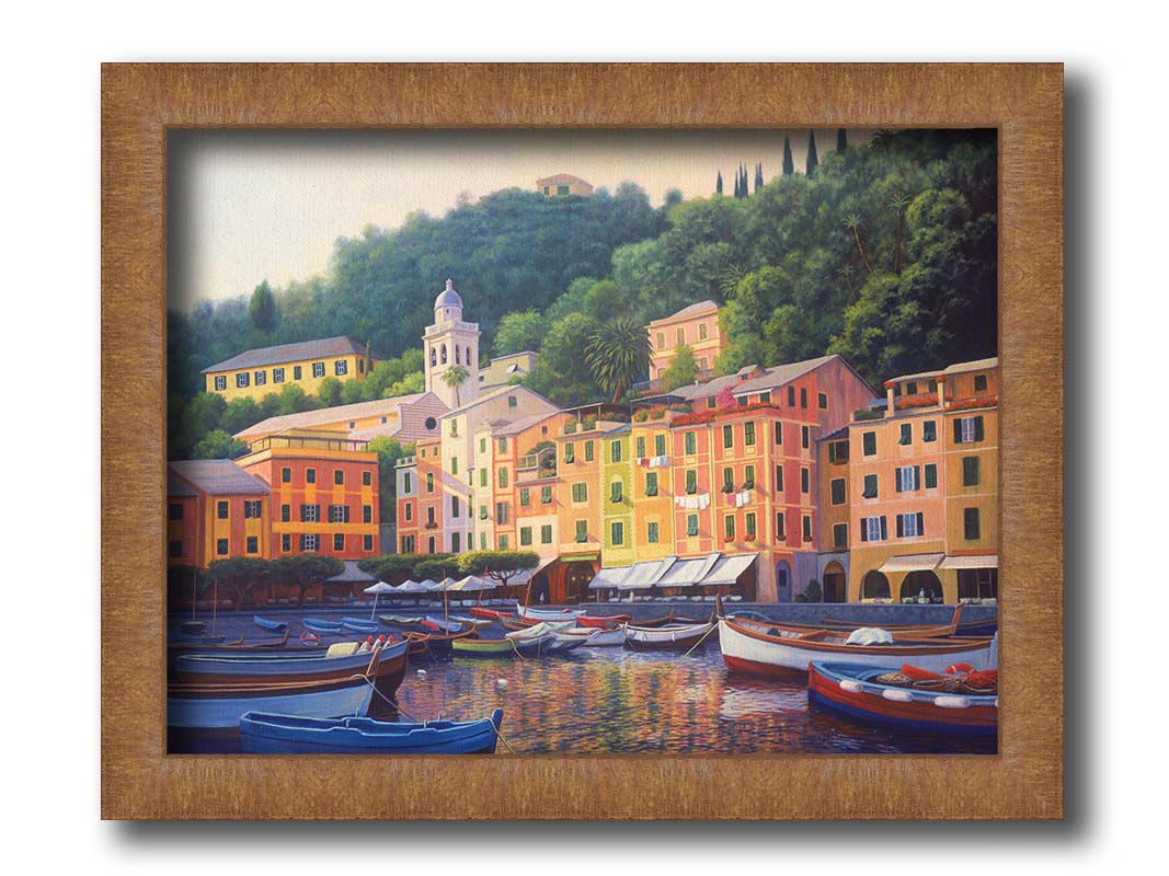 A painting of the colorful fishing town of Portofino. Many small boats are docked in the waters in the foreground, and the steep hills in the background are lush with trees. Printed on canvas and framed.