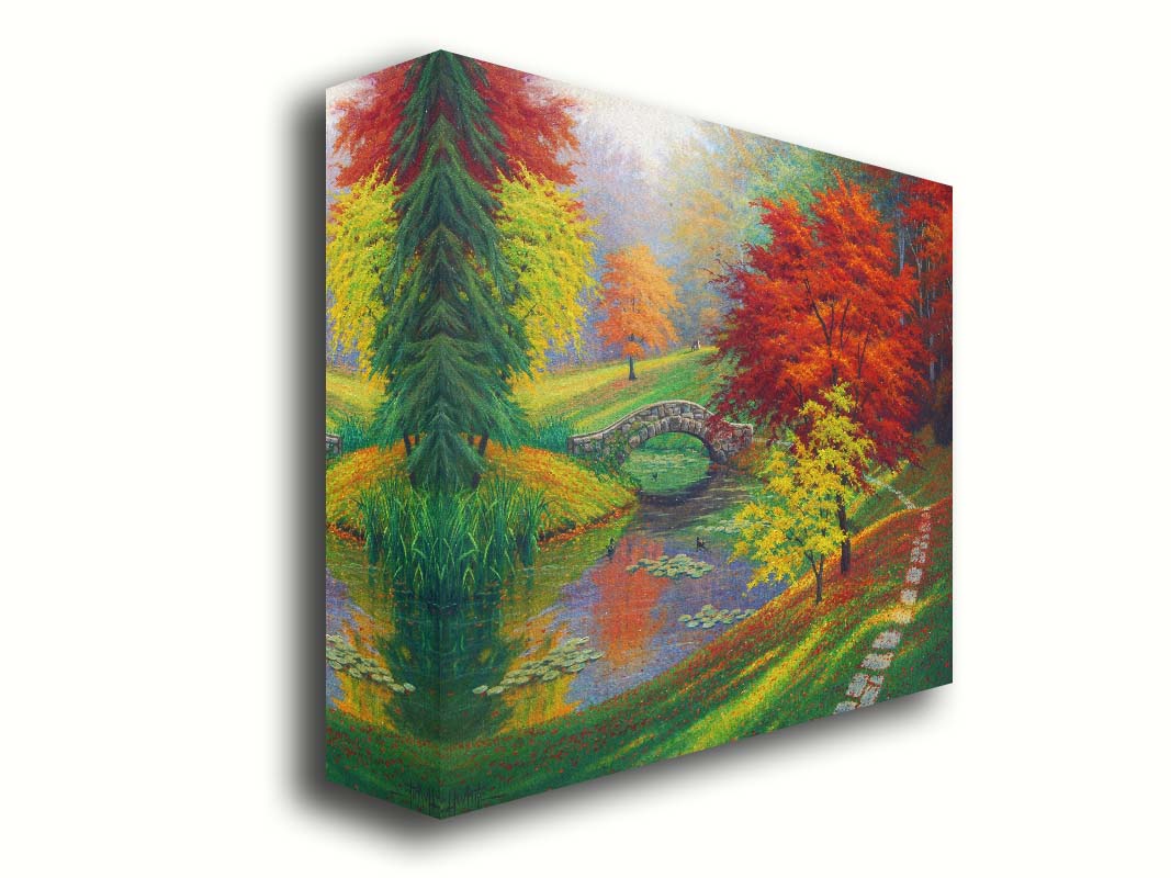 A painting of a fall park scene. Vibrant trees in hues of orange and red adorn the landscape while leaves gently fall. A stone bridge over a pond with lily pads and ducks. Printed on canvas.