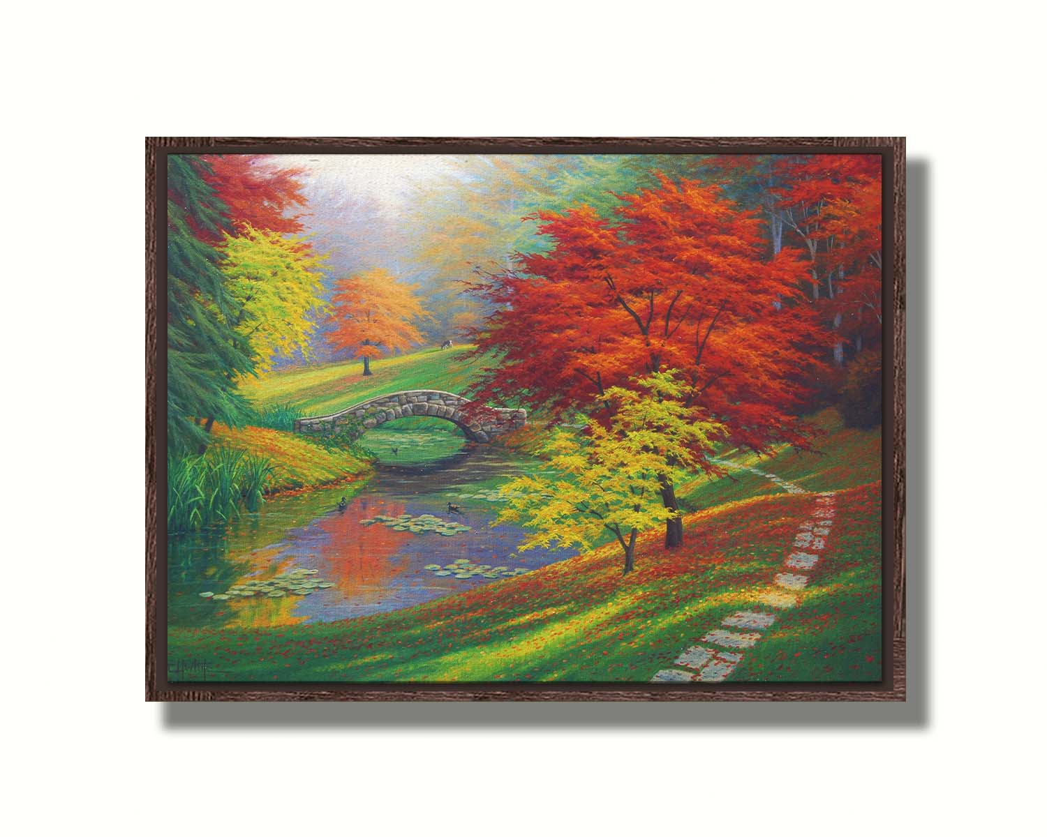 A painting of a fall park scene. Vibrant trees in hues of orange and red adorn the landscape while leaves gently fall. A stone bridge over a pond with lily pads and ducks. Printed on canvas in a float frame.