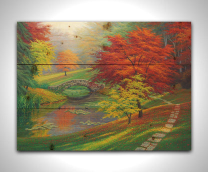 A painting of a fall park scene. Vibrant trees in hues of orange and red adorn the landscape while leaves gently fall. A stone bridge over a pond with lily pads and ducks. Printed on a wood pallet.