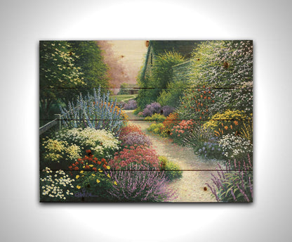 A painting of a gravel path through a garden with dense, colorful growths of flowers. The path and garden borders lead to cozy cottages. Printed on a wood pallet.