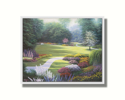 A painting of a sunny park. The open space of the grassy lawn is bordered by an abundance of colorful flowers and surrounding by trees. Printed on canvas in a float frame.