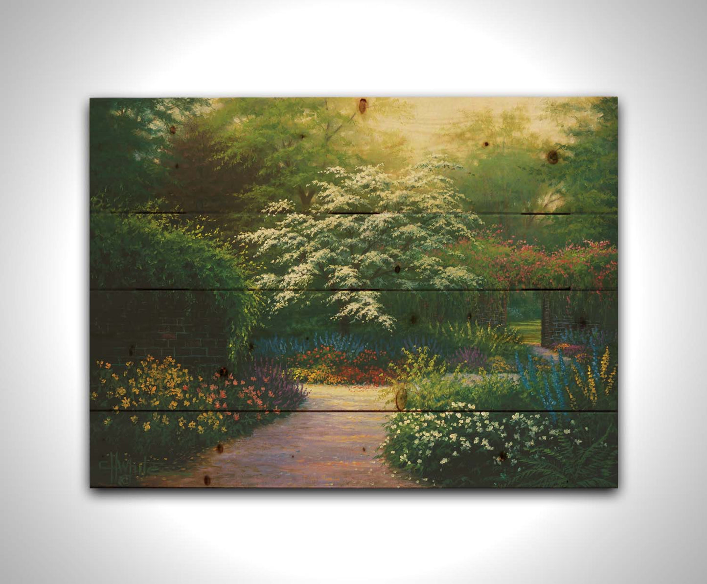 A painting of a brick wall surrounding a flower garden in a full spectrum of colors. A tree blossoming white stands central in contrast to the colorful scene. Printed on a wood pallet.