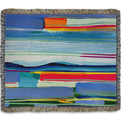 A woven throw blanket designed with an abstract painting of colorful horizontal lines. The blue and orange are reminiscent of a sun setting over the sea. 