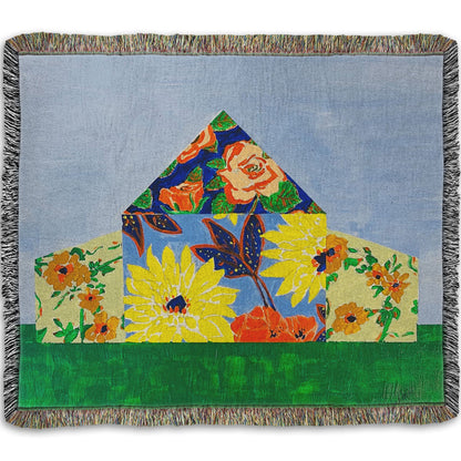 A woven throw blanket designed with an abstract painting of a barn silhouette formed of flower patterns, sitting on a green ground plane against a pale blue sky.