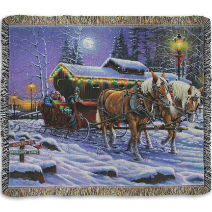 A woven throw blanket printed with a painting of people on a horse-drawn sleigh ride around a lake during Christmas.
