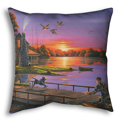 A throw pillow designed with a painting of a soldier returning home to his house on the lake, being greeted by his family and dogs. Geese fly overhead into the sunset. 