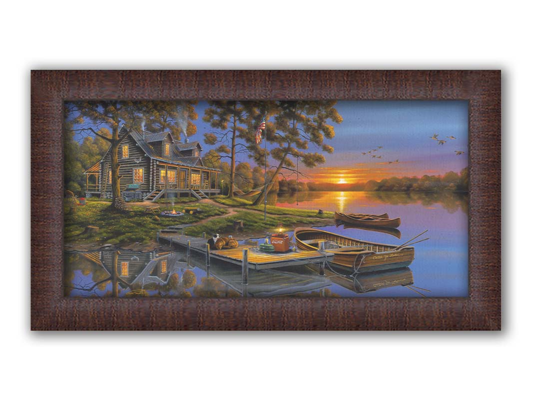 A painting of an American lakeside cabin at sunset, with boats on the water and geese overhead. Printed on canvas and framed.