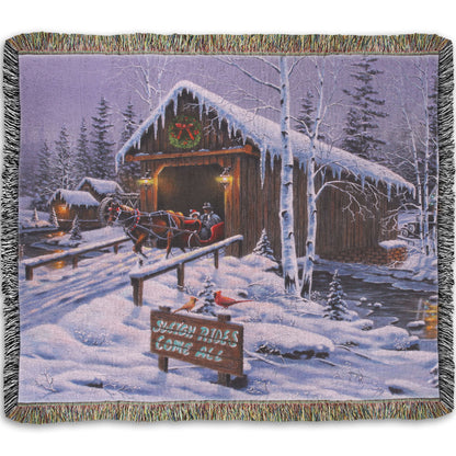 A woven throw blanket designed with a painting of people going for a ride in a horse-drawn sleigh on a snowy night.
