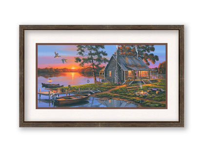 A painting of a lakeside cabin in a deciduous forest of the United States. The sunset is reflected by the water, where several small boats are docked. A lit campfire, deer, geese, and dog bring extra life to the scene. Printed on paper, matted, and framed.