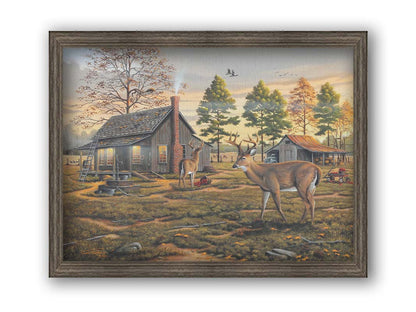 A painting of a farmhouse scene, featuring a fenced field, wood cabin, and an accompanying shed. In the foreground, deer are eating apples from wagons and baskets in the yard. Printed on canvas and framed.