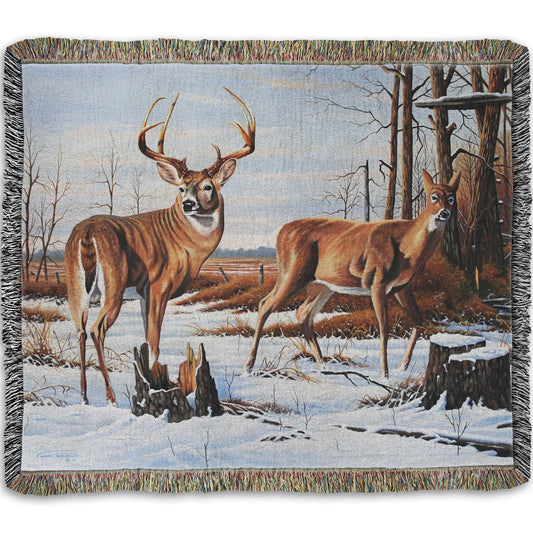 Woven throw blanket designed with deer walking through the snow between the woods and a field.